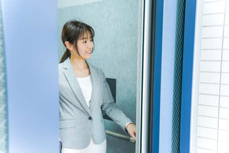 Young business woman standing in front of elevator and looking at the doorの写真素材