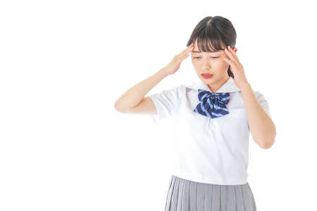 A high school girl in a student uniform taking a headache shot in the studioの写真素材