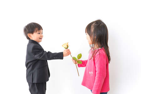 Child receiving a flower from another child in front of a white backgroundの写真素材