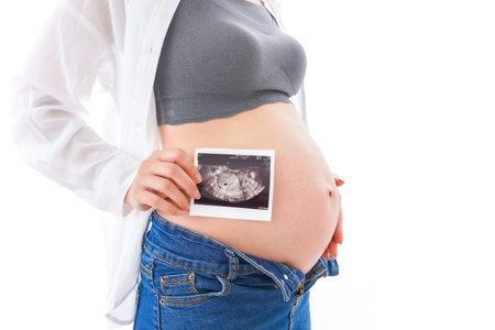 Pregnant woman holding ultrasound scan on white background, closeup