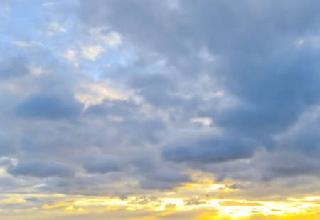 Yellow shining sun during sunset with blue cloudy skyの写真素材