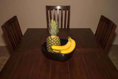 A fruit bowl on a rustic dark wooden dinner table with chairsの写真素材