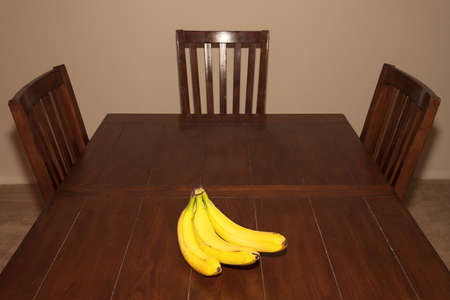 A bunch of bananas on a rustic dinner table with chairs aroundの写真素材