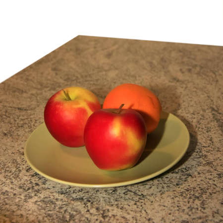 Two apples and an orange on a plate on a kitchen tableの写真素材
