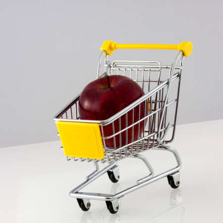 A partly yellow shopping cart with a red apple in itの写真素材