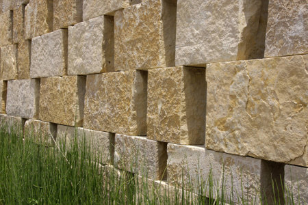 Background of a beige natural stone wall with green grass in frontの写真素材