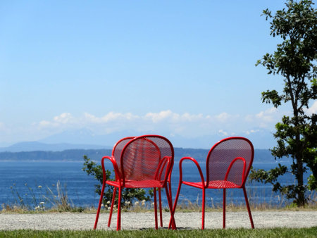 Three empty red metal chairs facing the oceanの写真素材