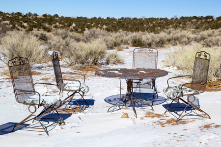 Four empty garden chairs around a table in the desert with snowの写真素材