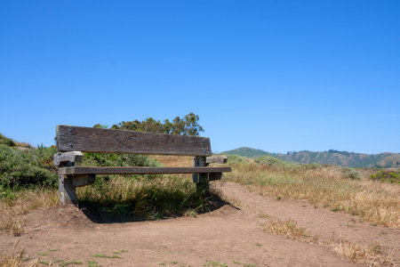 A wooden bench on top of a hill under blue and sunny skyの写真素材