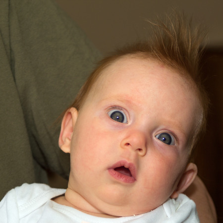 An almost four month old baby with very opened eyes looking into the cameraの写真素材