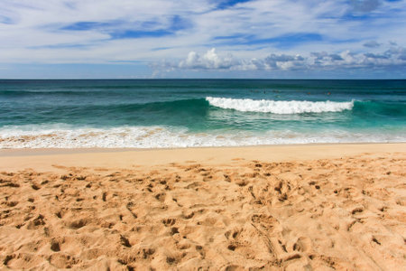 A sandy beach with ocean and incoming waves and cloudy sky in background の写真素材