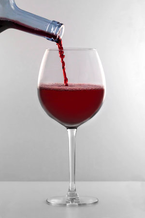 Pouring red wine into a glass from a blue bottleの写真素材