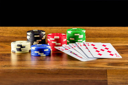 Chips and playing cards on a dusty wooden table with black background