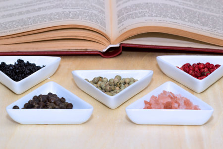 Variety of peppercorns and salt with open cook book in backgroundの写真素材