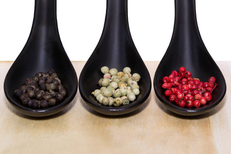Three types of peppercorns on black spoonsの写真素材