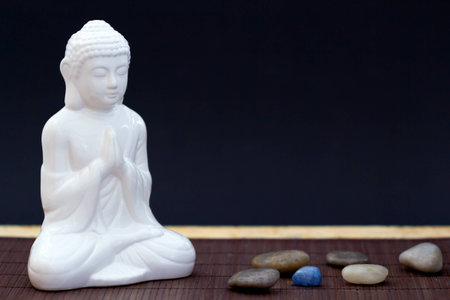 White figure in meditation pose with pebbles and one blue stoneの写真素材