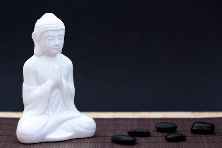 White figure in meditation pose with black pebblesの写真素材