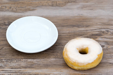 Glazed donut next to an empty plate from above - foodshot with slightly blurred background and copy spaceの写真素材