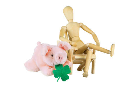 A wooden doll is sitting on a chair next to a plush piggy with shamrock over whiteの写真素材