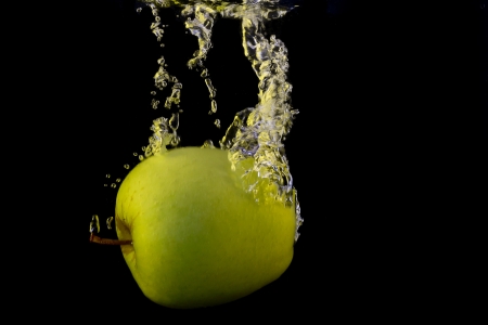 Green apple in yellow splash isolated on black backgroundの写真素材
