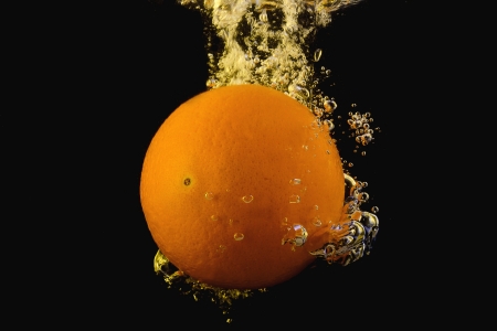 Bright ripe orange dropping into water as it breaks the surfaceの写真素材