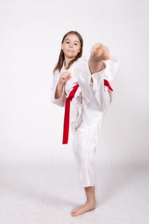 Karate young girl in a kimono with a red belt kicking up, isolated on white backgroundの写真素材