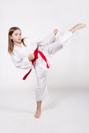 Karate young girl in a kimono with a red belt kicking up, isolated on white backgroundの写真素材