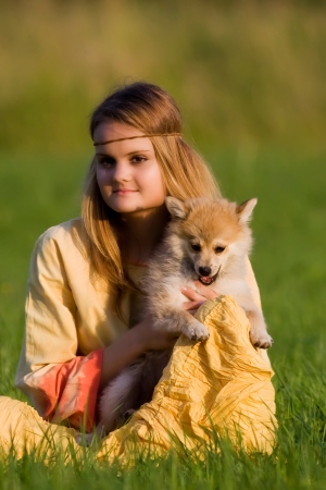 Young hippie girl sitting with Spitz dog on the grass in a meadow in a yellow dressの写真素材