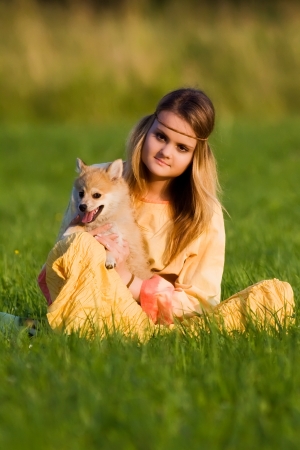 Young hippie girl sitting with Spitz dog on the grass in a meadow in a yellow dressの写真素材