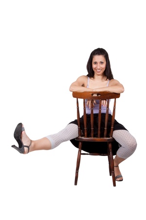 Long-haired brunette woman is sitting on a chair, she laughs, has one leg outstretched forward, isolated on a white backgroundの写真素材