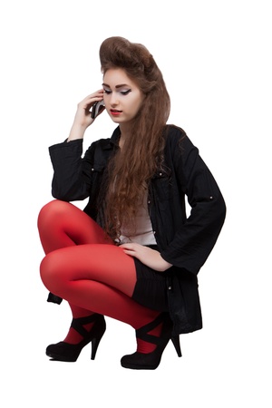 Teenage girl in black and red dress is squatting with phone in hand, isolated on white backgroundの写真素材