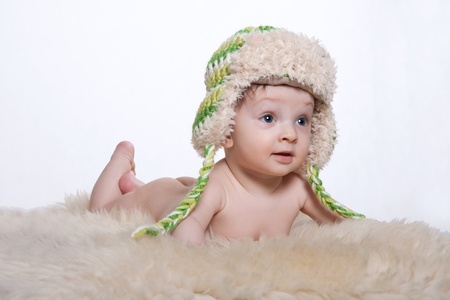 Little baby boy lying on stomach on woolen fleece on his head is cap on a white backgroundの写真素材
