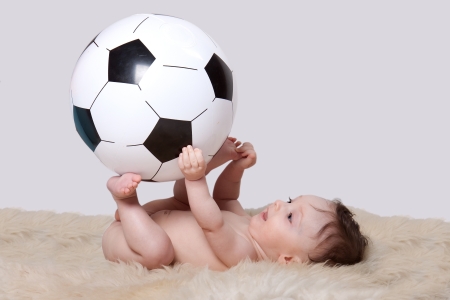 Little baby boy lying on her back on woolen fleece holding big soccer ball on white backgroundの写真素材