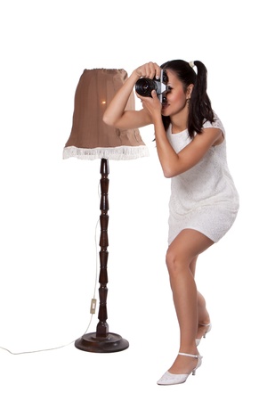 Retro woman in white dress, standing next to the old lamp and take pictures, with old camera isolated on white backgroundの写真素材