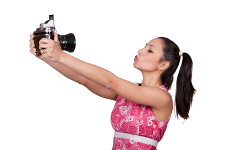 Retro girl in a pink dress, holding in his hands an old camera, a photographer himself, makes a grimace, isolated on white backgroundの写真素材