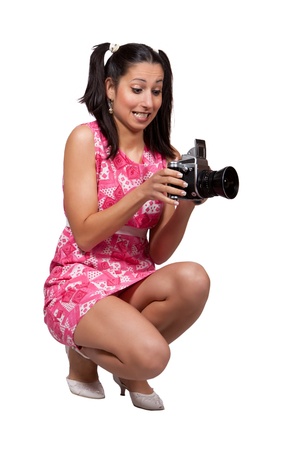 Retro girl in a pink dress, holding in his hands an old camera, is squatting, photographing, isolated on white backgroundの写真素材