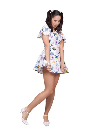 A girl with pigtails in colorful retro dress is embarrassed, she holds her skirt, isolated on white backgroundの写真素材