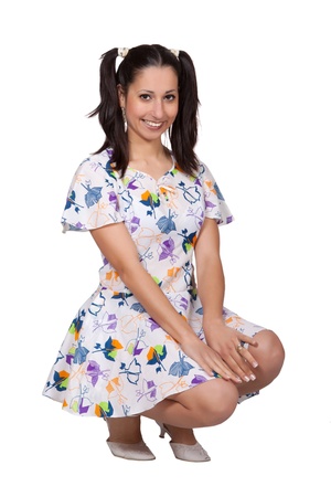 A girl with pigtails in colorful retro dress, is squatting and laughing, isolated on white backgroundの写真素材