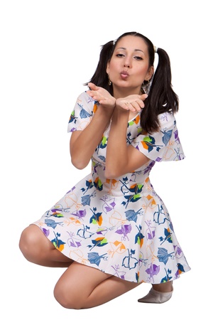 A girl with pigtails in colorful retro dress, is squatting and laughing, isolated on white backgroundの写真素材