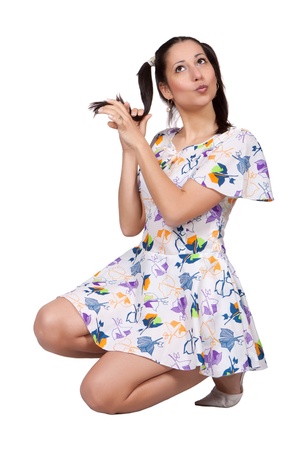 A girl with pigtails in colorful retro dress, is squatting and plays with braid, isolated on white backgroundの写真素材