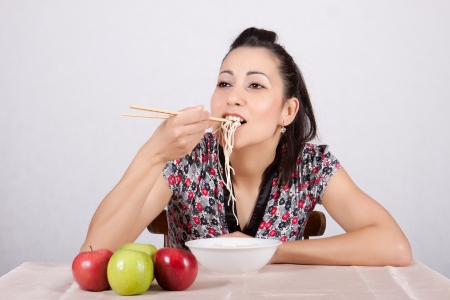 Woman eat a bowl of Chinese noodles with chopsticks, at a table with applesの写真素材