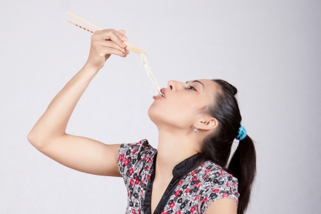 A woman puts into the mouth of Chinese noodles with chopsticksの写真素材