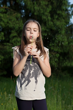 Teens girl blowing dandelion in the meadowの写真素材