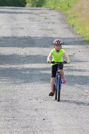 Girl teens in neon yellow shirt and a red helmet riding a bike down the old forest roadの写真素材