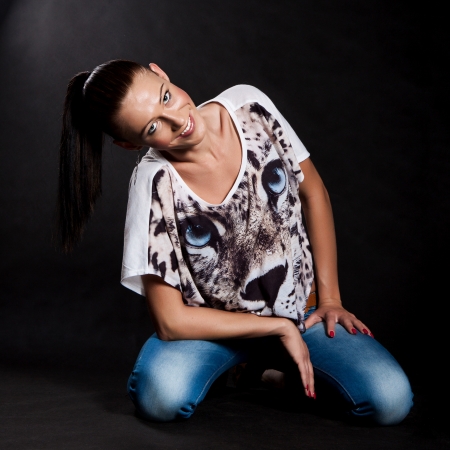 Woman with long hair in a shirt with a tiger and jeans kneeling and smiling, on black backgroundの写真素材