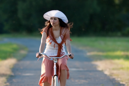 Woman in orange skirt and white hat riding on a retro bike in meadow view from the frontの写真素材