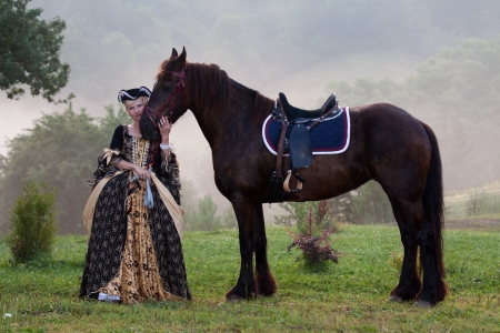 Woman in royal baroque dress, standing next to a horse in the fogの写真素材