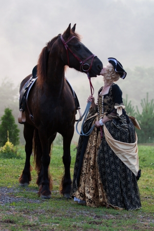 Woman in royal baroque dress, kissing a horse in the fogの写真素材
