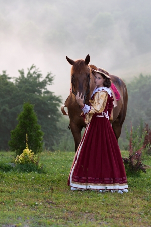 Girl in baroque dress royal, next to a horse in the fogの写真素材