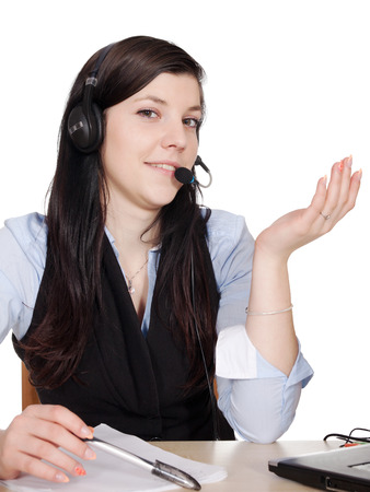 Young woman with headsets phone, and shows with hand and sitting at the table with laptop, isolated on white backgroundの写真素材
